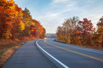 Fototapeta premium Cars travel along a curve in the road near the Mississippi River in Brainerd Minnesota on an autumn morning