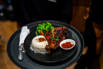 Ayam Bakar kecap, Roasted Chicken with Soy Sauce, Herb and Spice from Indonesia. served with chili sauce (sambal), cucumber and tomato