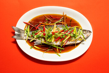Chinese Lunar New Year festive table. Cantonese-Style recipes  Sea bass or Spigola fish steamed with ginger, red peppers in soy sauce