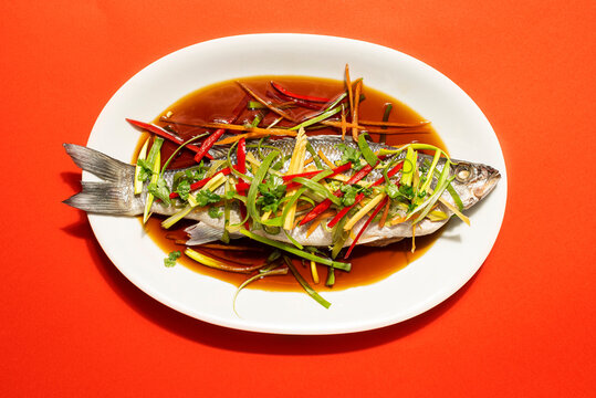 Chinese Lunar New Year festive table. Cantonese-Style recipes  Sea bass or Spigola fish steamed with ginger, red peppers in soy sauce