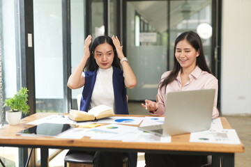 Happy Asian business people working together using laptop and tablet in office.