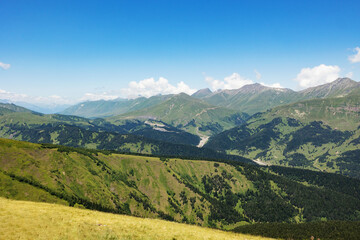 Scenic views on mountain peaks and valley at summer. Green meadows and forests, slopes, hilly countryside, blue sky with clouds. Beautiful landscape, travel background, wallpapers and banner.