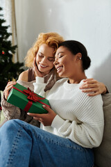 A loving lesbian couple shares a heartfelt gift at home during the holidays.