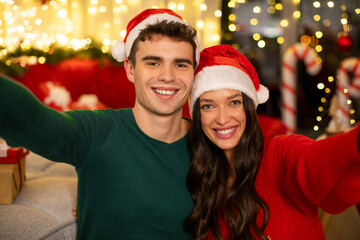 Xmas selfie. Happy young European couple taking self-portrait with Christmas garlands and decorations on background, celebrating winter holidays together