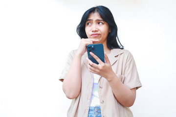Fototapeta premium thoughtful asian woman looks confused using smartphone wearing casual clothes isolated on white background