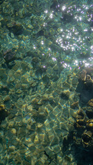 The water is clear and calm, with ripples and reflections of the sky and rocks