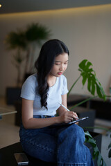 Asian teenage student woman doing assignment homework and writing notes on digital tablet after...