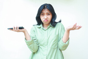 portrait of confused asian woman wearing green shirt shrug shoulders and spreads palms holding...