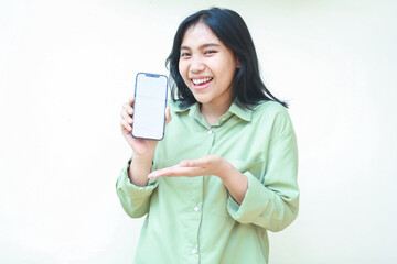 pleased delighted confident asian woman with dark hair showing blank screen of smartphone wearing green over size shirt standing isolated white background, introduce good product sale promotion