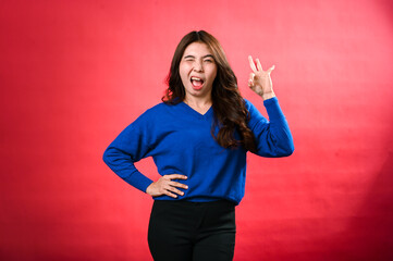 An Asian woman in a blue sweater and black pants smiles while winking and making an 