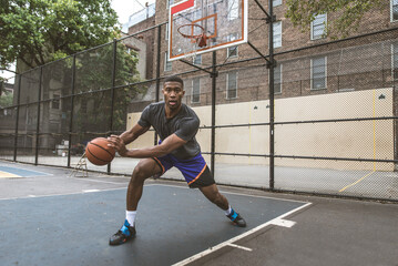 Fototapeta premium African american basketball player training outdoors - Sportive man playing basketball on a outdoor court in New York City