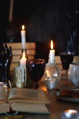 Books, lit candles, red wine, snacks and various deocration on the table. Dark academia or Halloween concept. Selective focus.