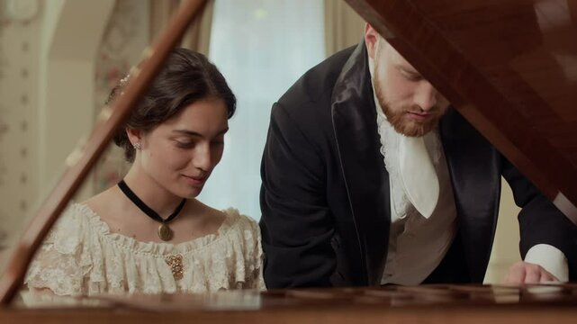 Young Victorian-era woman in lace dress and vintage choker on her neck learning to play piano with male teacher in formal attire giving instructions