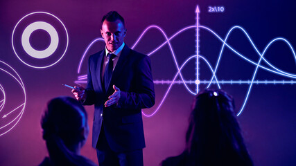Male presenter engages audience with interactive visual data projections on glowing background. Concept of presentation, training, meeting, leadership, analysis. Copy space for ad.