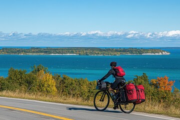 Fototapeta premium A cyclist rides along a scenic route with vibrant trees and a blue lake in the background.