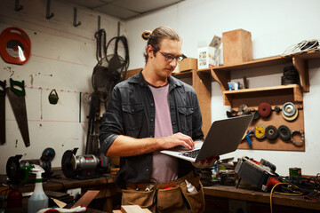 Man, woodwork or carpenter with laptop for design, precision or innovation in garage. Young, male person or artisan with computer for stock, inventory or DIY project in carpentry business at workshop