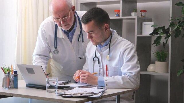 An elderly doctor in the office, talking with a young intern doctor, discussing the patient's condition and his further treatment, through discussion they come to a consensus regarding the diagnosis a