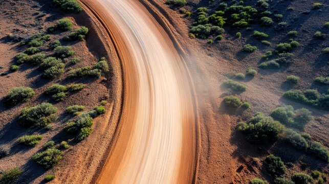 A curved dirt road illuminated by bright sunlight, lined by green bushes, creating a scenic path through the landscape, hinting at the journey and discovery.