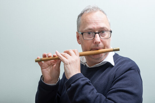 Middle aged man, casually dressed, greying hair, wearing glasses, experienced musician, playing traditional box wood fife.