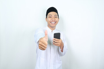 smiling asian muslim man showing thumbs up with holding phone isolated