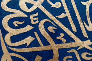 A piece of golden Arabic letters on a blue background, creating a striking contrast between the...