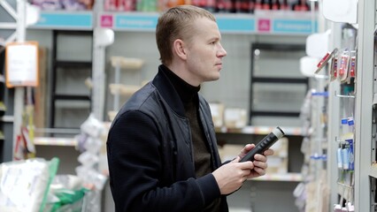 A man chooses hygiene products in a supermarket, shelves with shampoos. Shopper carefully selects a hair conditioner from the supermarket shelf and reads the label on the bottle