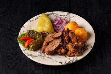 cold cuts. stuffed peppers, stuffed grape leaves, shish kebab, fried fish, potatoes and fresh onions on a black wooden background