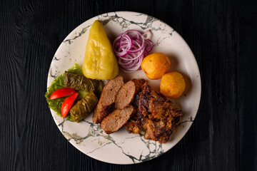 cold cuts. stuffed peppers, stuffed grape leaves, shish kebab, fried fish, potatoes and fresh onions on a black wooden background