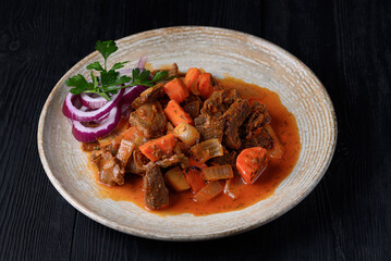 roast meat with vegetables in juice, fresh onions. on a black wooden background