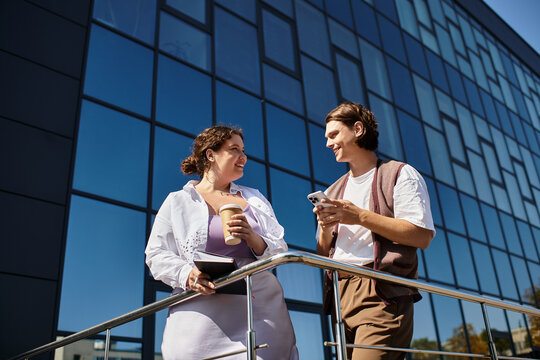 A young plus size woman and her male friend share laughs while holding drinks on a sunny day.