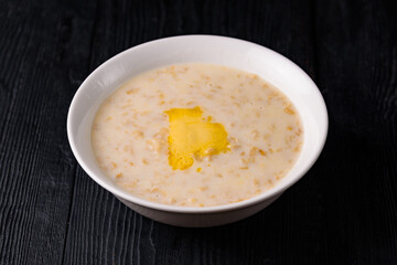 oatmeal porridge with milk and butter. on a black wooden background
