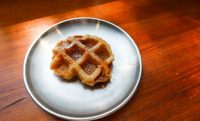 close up of freshly baked Belgium waffle on a metal steel plate with sugar powder