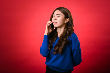 An Asian woman in a blue sweater holds a phone to her ear, with her eyes closed and an expression...