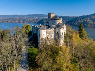 Naklejka premium Poland. Medieval castle in Niedzica, dating to 14th century (upper castle) in autumn in October. Trees in beautiful fall colors. Sunrise light. Artificial Czorsztyn lake on Dunajec river. Aerial view