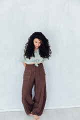 Curly brunette woman standing near a white wall