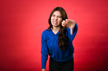 An Asian woman in a blue sweater showing a displeased facial expression, giving a thumbs-down...