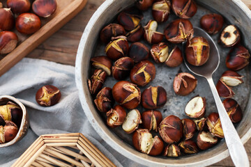 wooden table topped with trays of fresh and toasted chestnuts a person holding roasted chestnuts