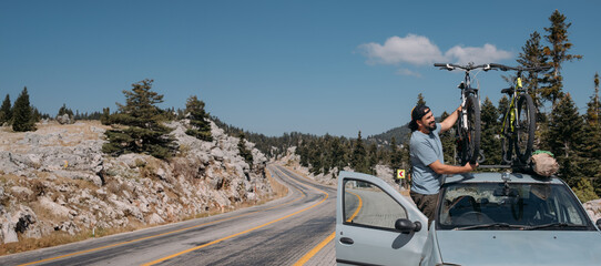 A man puts bicycles on the roof of a car on a mountain road.