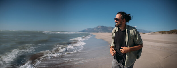 A young man walks along a sandy beach along the edge of the sea surf.
