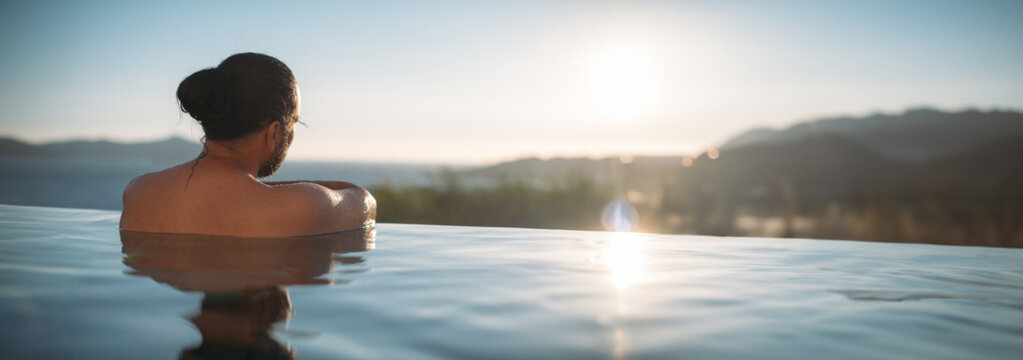 A young sexy man is relaxing in an open-air pool at sunset.
