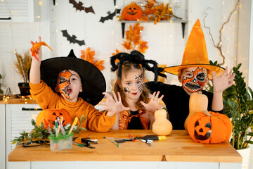Halloween, kids boys and a girl in festive costumes and makeup are preparing for Halloween at home in the kitchen by coloring and carving pumpkins and scaring everyone