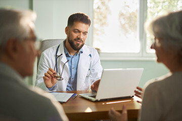 Obraz premium Young male doctor talking with a senior couple during an appointment in the office.