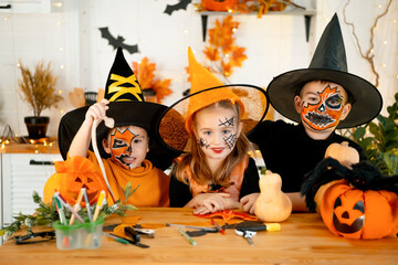 Halloween, kids boys and a girl in festive costumes and makeup are preparing for Halloween at home in the kitchen by coloring and carving pumpkins and scaring everyone