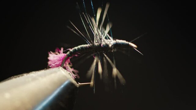 Handmade fishing fly in the vice on the solid studio background