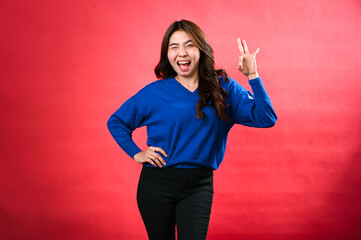 An Asian woman in a blue sweater and black pants smiles while winking and making an 