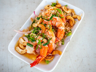 Shrimp spicy salad in Thai style, sour and chili spicy, serve with many Thai vegetables and herbs and cashew nut in white plate in restaurant