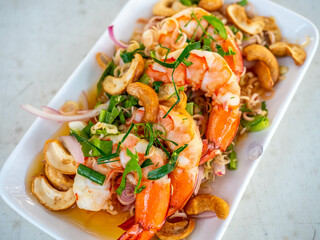 Shrimp spicy salad in Thai style, sour and chili spicy, serve with many Thai vegetables and herbs and cashew nut in white plate in restaurant