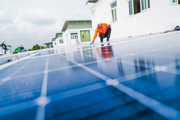 A worker in an orange safety jacket inspects solar panels on a rooftop, using a laptop to ensure...