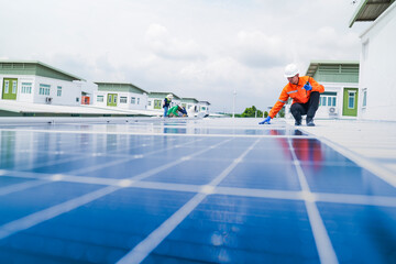 A worker in an orange safety jacket inspects solar panels on a rooftop, using a laptop to ensure...