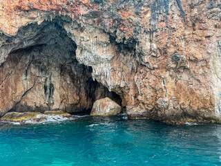 Boat trip with scenic view of large sea cave called Monastery caves near Himare, Vlore, Albania. Dramatic coastal landscape of Albanian Riviera with natural archway. Sightseeing on Mediterranean sea